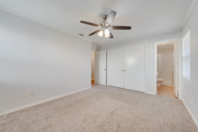 unfurnished bedroom featuring ensuite bathroom, crown molding, light colored carpet, a closet, and ceiling fan