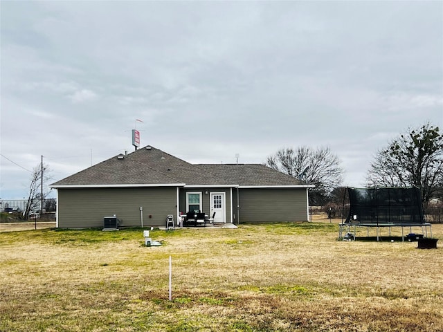 back of house featuring central air condition unit, a shingled roof, a trampoline, and a yard