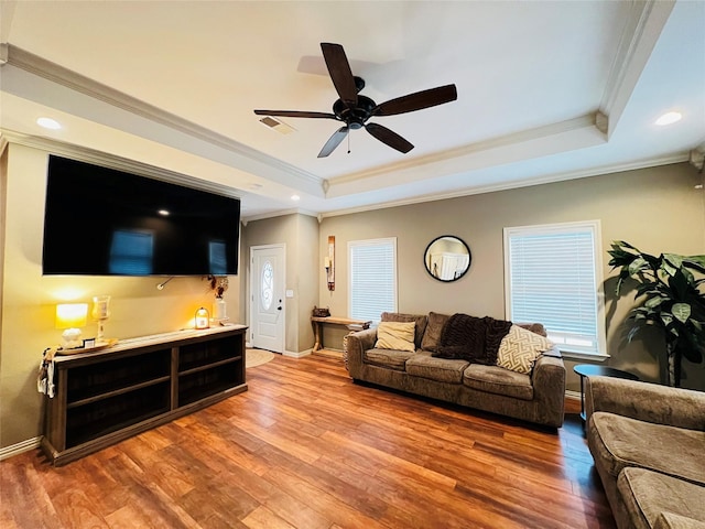 living area featuring ornamental molding, a tray ceiling, baseboards, and wood finished floors