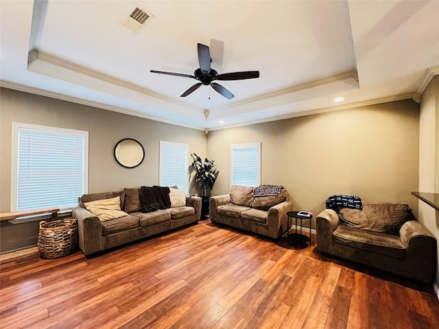 living area featuring a tray ceiling, light wood-style flooring, visible vents, and crown molding