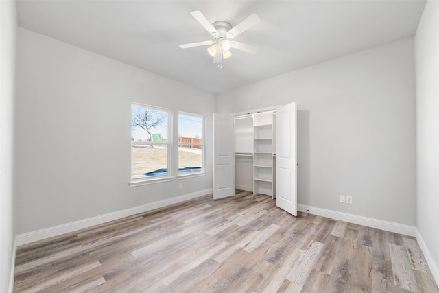 unfurnished bedroom featuring a barn door, light wood-type flooring, ceiling fan, and a closet