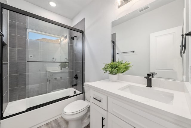 full bathroom with vanity, hardwood / wood-style floors, combined bath / shower with glass door, and toilet