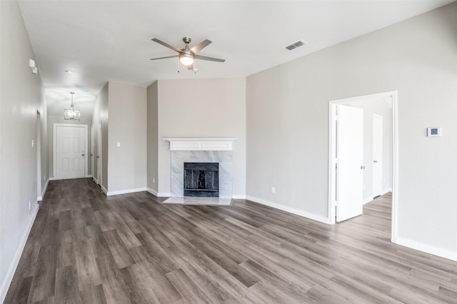 unfurnished living room featuring dark wood-type flooring, a high end fireplace, and ceiling fan with notable chandelier