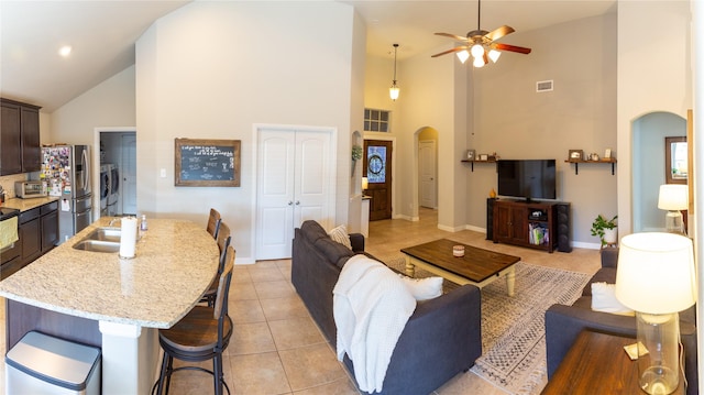 tiled living room with ceiling fan, washer and clothes dryer, and high vaulted ceiling