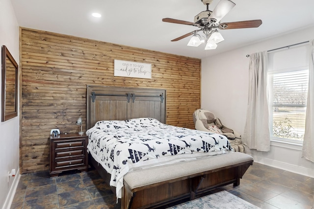 bedroom with ceiling fan, wood walls, stone finish floor, and baseboards