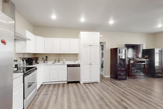 kitchen featuring light wood finished floors, stainless steel appliances, light countertops, white cabinetry, and a sink