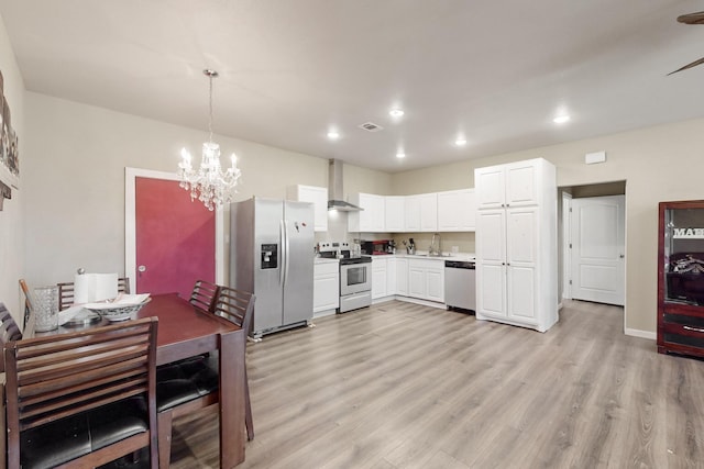 kitchen with light wood finished floors, stainless steel appliances, wall chimney range hood, and white cabinets