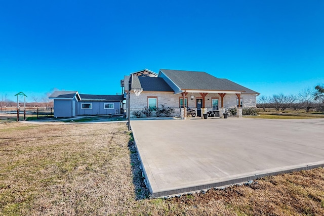 rear view of property with stone siding, covered porch, a lawn, and fence