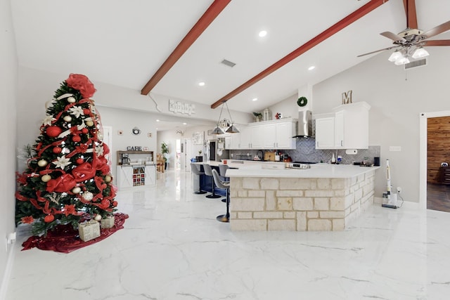 kitchen featuring white cabinets, marble finish floor, light countertops, wall chimney exhaust hood, and beamed ceiling