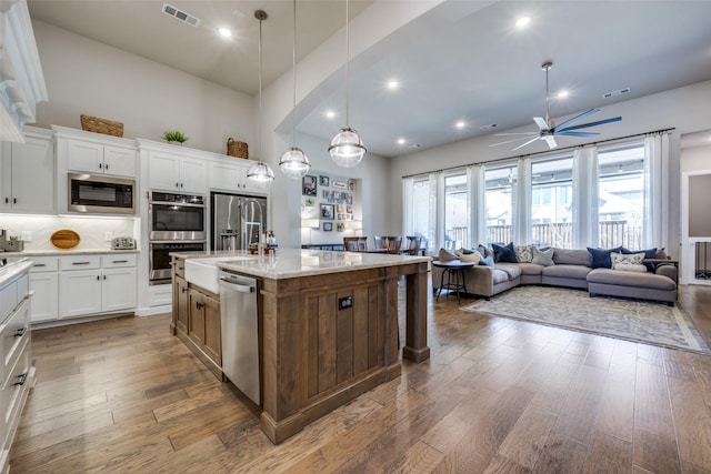 kitchen with white cabinetry, light stone counters, pendant lighting, stainless steel appliances, and a kitchen island with sink