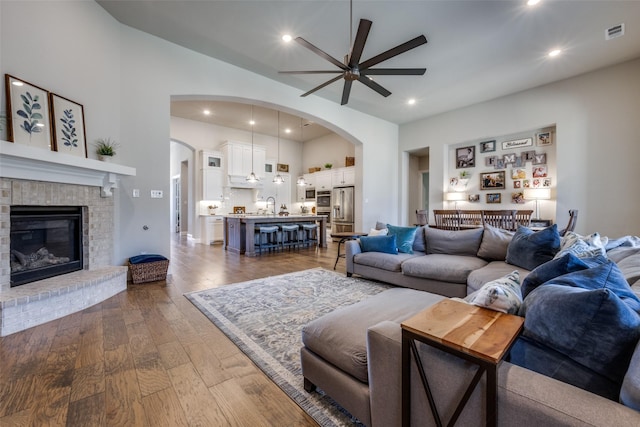 living room with ceiling fan, dark hardwood / wood-style floors, sink, and a brick fireplace