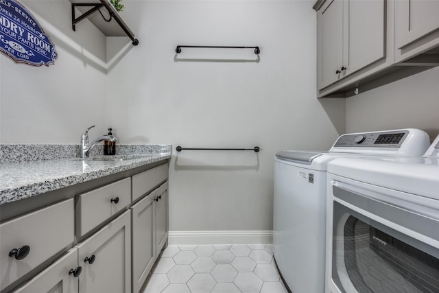 laundry area with sink, light tile patterned floors, washing machine and dryer, and cabinets