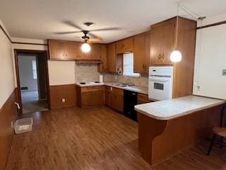 kitchen featuring wood-type flooring, oven, a kitchen bar, ceiling fan, and kitchen peninsula