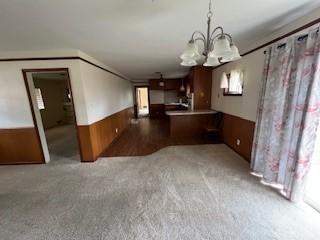 interior space with pendant lighting, wooden walls, carpet flooring, a notable chandelier, and kitchen peninsula