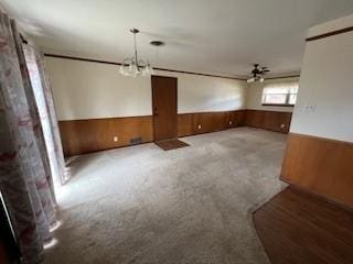 carpeted empty room with ceiling fan with notable chandelier and wood walls