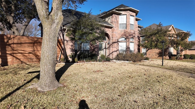 view of front facade featuring a front yard, brick siding, and fence