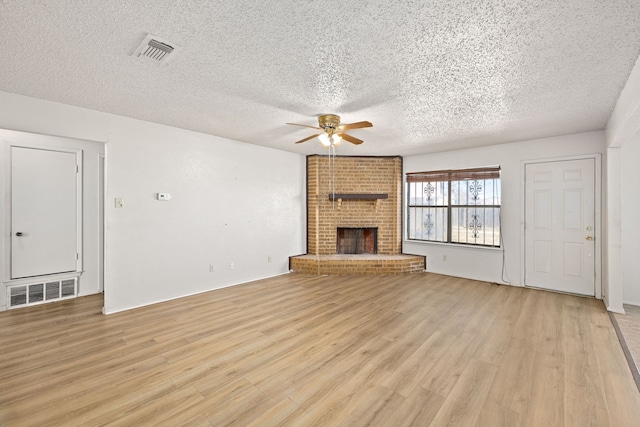 unfurnished living room with ceiling fan, a brick fireplace, a textured ceiling, and light hardwood / wood-style floors