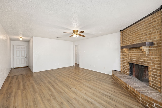 unfurnished living room with ceiling fan, a fireplace, a textured ceiling, and light wood-type flooring