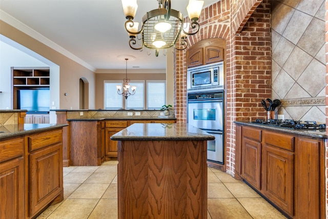 kitchen featuring decorative light fixtures, ornamental molding, a kitchen island, a notable chandelier, and stainless steel appliances