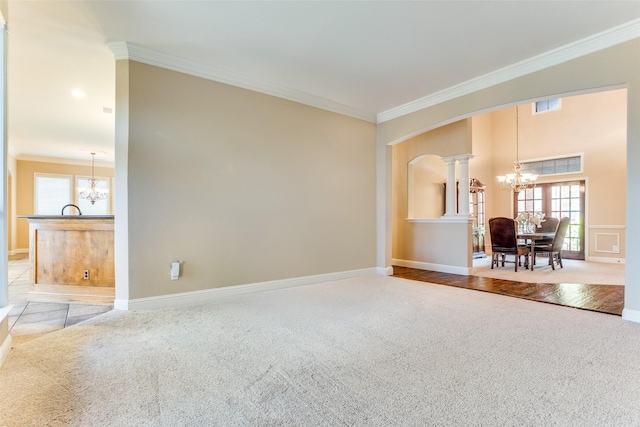 unfurnished living room featuring carpet floors, ornamental molding, a chandelier, and ornate columns