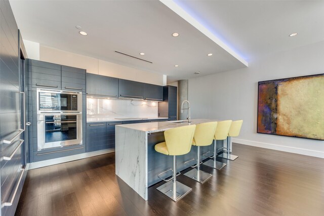 2408 Victory Park Ln Unit 1037, Dallas, TX 75219 - kitchen featuring appliances with stainless steel finishes, dark wood-type flooring, modern cabinets, a breakfast bar, and a center island with sink
