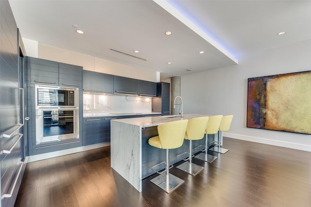 kitchen with tasteful backsplash, black appliances, a kitchen breakfast bar, and a center island with sink