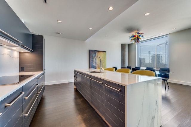 kitchen featuring sink, backsplash, black electric stovetop, a center island with sink, and dark hardwood / wood-style flooring