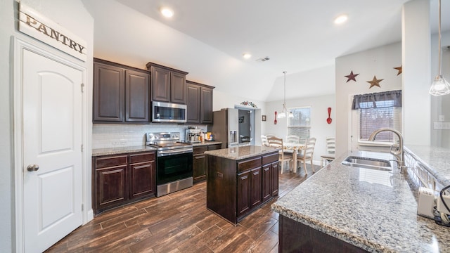 kitchen with sink, a center island, vaulted ceiling, hanging light fixtures, and appliances with stainless steel finishes