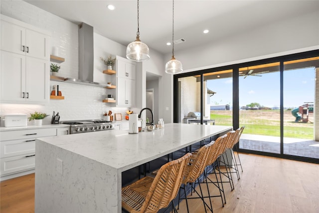 kitchen with range hood, white cabinetry, stove, a kitchen island with sink, and light stone counters