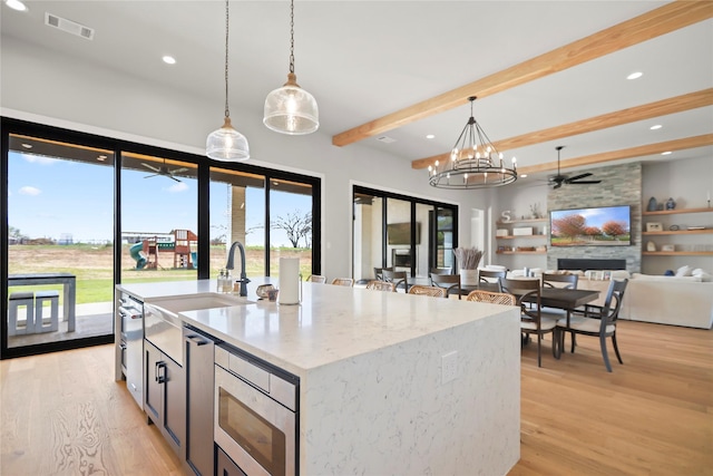 kitchen with stainless steel microwave, decorative light fixtures, a fireplace, and an island with sink