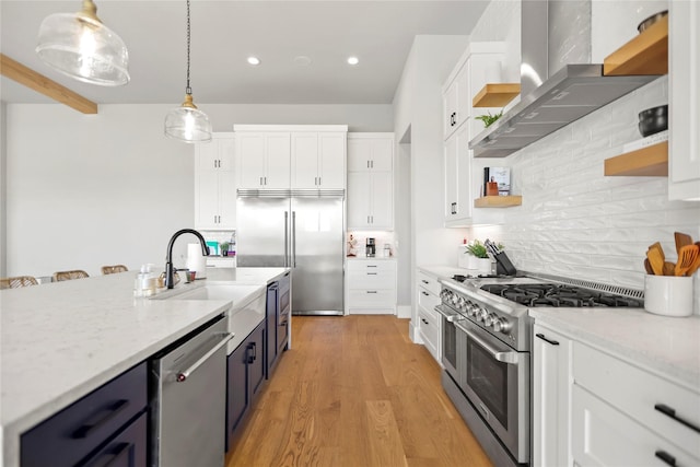 kitchen featuring sink, high quality appliances, white cabinets, pendant lighting, and wall chimney range hood