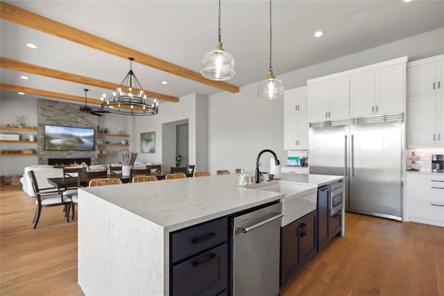 kitchen with white cabinetry, built in appliances, decorative light fixtures, a center island with sink, and a large fireplace