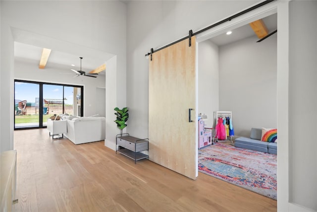 hallway with beamed ceiling, a barn door, and light hardwood / wood-style flooring