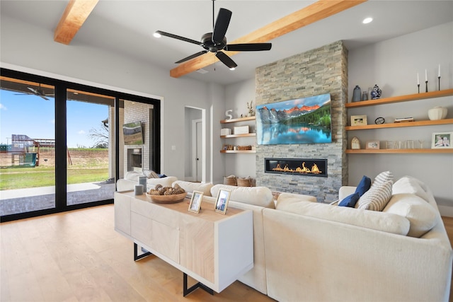 living room featuring beam ceiling, a stone fireplace, light hardwood / wood-style floors, and ceiling fan