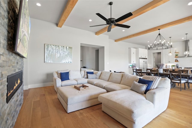 living room featuring beamed ceiling, a stone fireplace, ceiling fan with notable chandelier, and light hardwood / wood-style floors