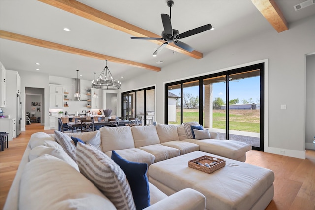 living room with beamed ceiling, ceiling fan with notable chandelier, and light wood-type flooring