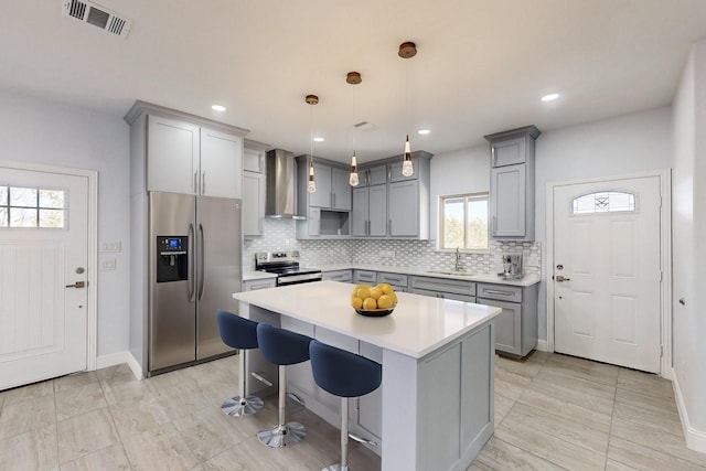 kitchen featuring a center island, hanging light fixtures, a kitchen breakfast bar, stainless steel appliances, and wall chimney range hood