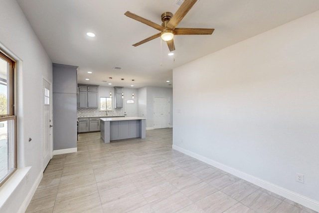 kitchen with pendant lighting, ceiling fan, gray cabinetry, a center island, and decorative backsplash