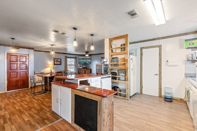 kitchen with white cabinetry, ornamental molding, decorative light fixtures, and light hardwood / wood-style floors