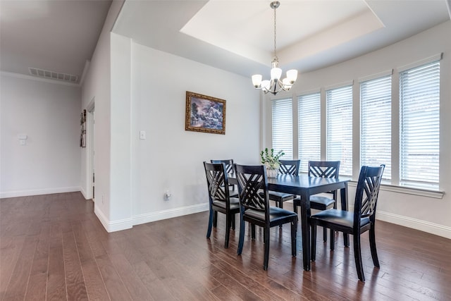 dining area with a raised ceiling, an inviting chandelier, and dark hardwood / wood-style flooring