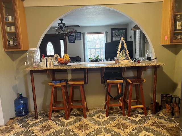 bar featuring arched walkways, tile patterned flooring, ceiling fan, and a textured ceiling