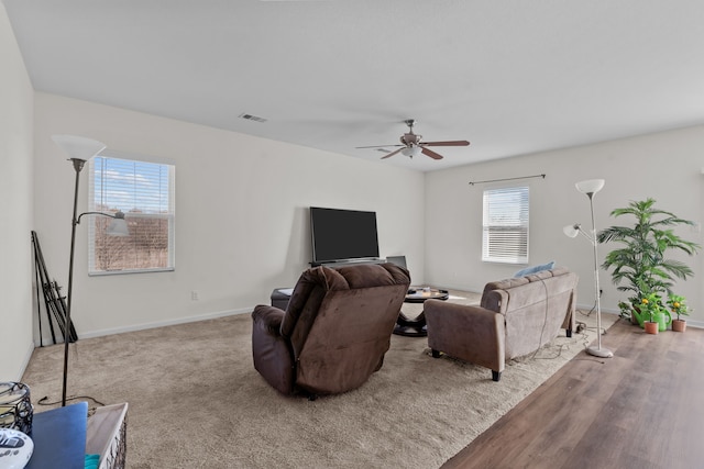 living area with ceiling fan, wood finished floors, visible vents, and baseboards