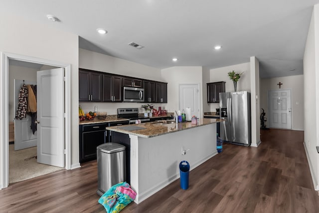 kitchen featuring stone countertops, a center island with sink, visible vents, dark wood finished floors, and stainless steel appliances