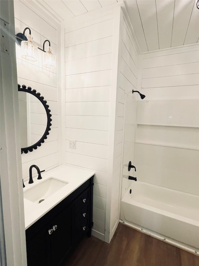 bathroom featuring vanity, hardwood / wood-style floors, wooden walls, and shower / washtub combination