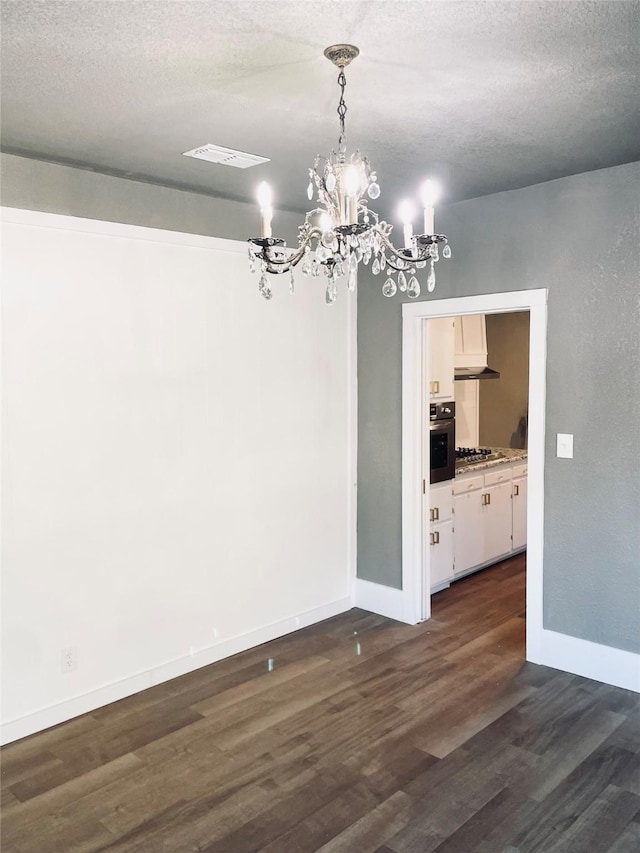 unfurnished dining area featuring dark hardwood / wood-style floors, an inviting chandelier, and a textured ceiling