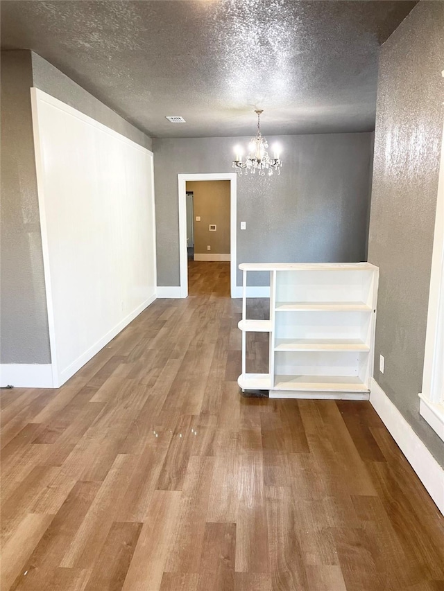 empty room with hardwood / wood-style flooring, a textured ceiling, and an inviting chandelier