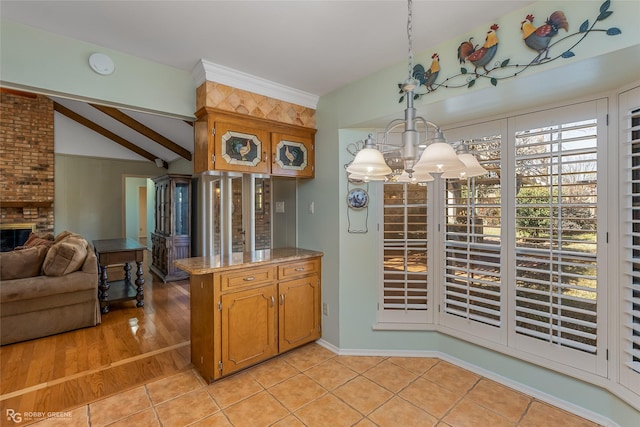 kitchen featuring pendant lighting, light tile patterned floors, vaulted ceiling with beams, a fireplace, and a chandelier