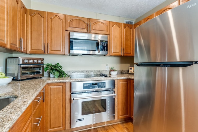 kitchen featuring light stone counters, appliances with stainless steel finishes, a textured ceiling, and light wood-type flooring