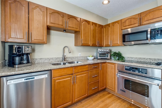 kitchen with appliances with stainless steel finishes, sink, light stone countertops, a textured ceiling, and light hardwood / wood-style flooring