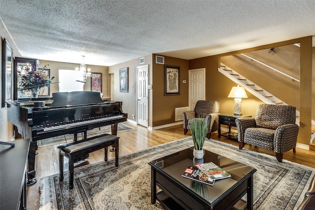 living area with an inviting chandelier, hardwood / wood-style flooring, and a textured ceiling